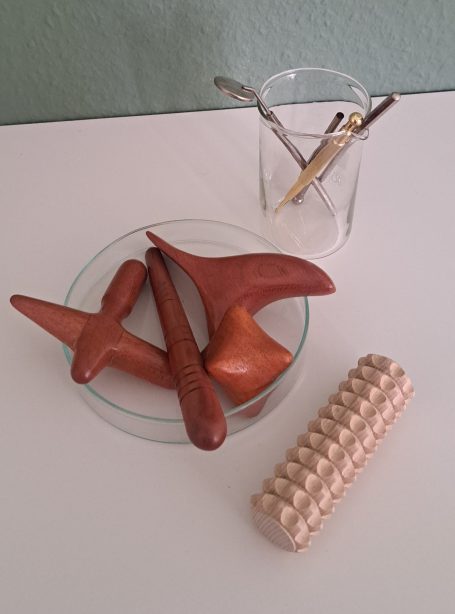 Heilpraktische Utensilien aus Holz und Metall in Glasgefäßen angeordnet.