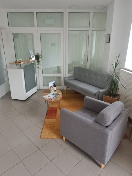 Raum mit Empfangstresen, zweisitziger Couch, einem Sessel und kleinem Tisch.