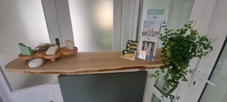 Ein Empfangstresen mit Grünpflanze, Prospektmaterial und einigen, dekorativ aufgestellten Seifen und ähnlichen Produktmustern.